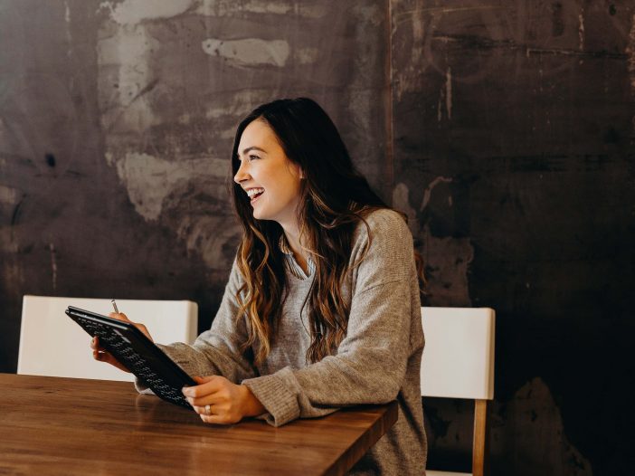 A young woman completes a survey by tablet while sitting in a modern, industrial conference room.